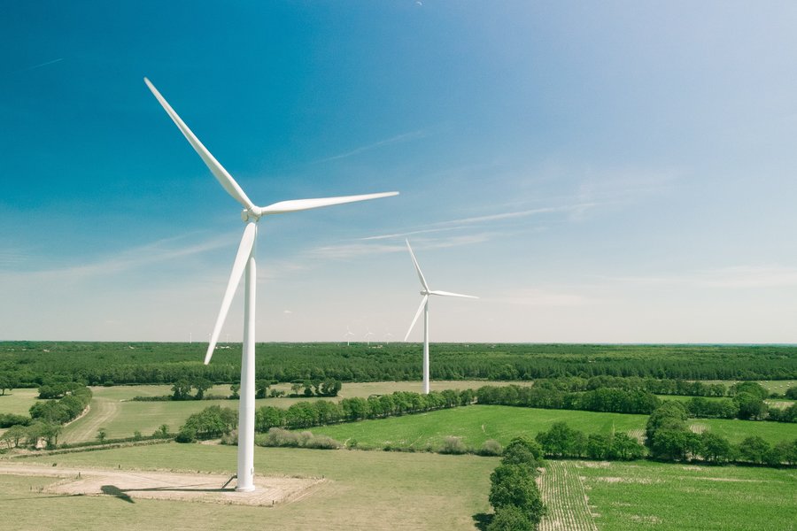 Ein Foto von einer weiten, hügellosen Landschaft unter blauem Himmel. Darauf stehen zwei Windräder.